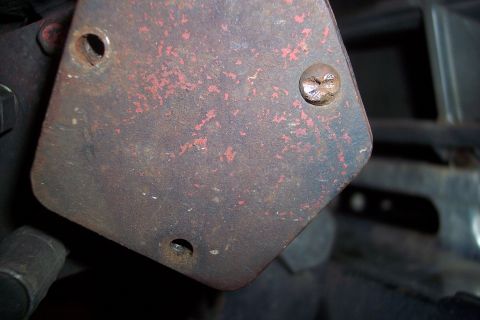 1973 Ford F-250 - A close-up view of a rusty, red-painted metal plate with two visible screw holes and one screw. The plate appears to be part of a vehicle's…