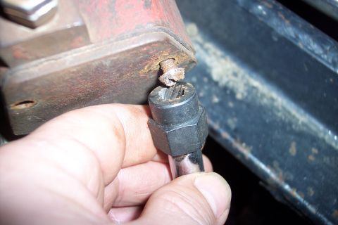 1973 Ford F-250 - A hand holds a damaged bolt head with a bolt extractor socket attached, ready to be removed from a rusty metal bracket.