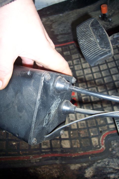 1973 Ford F-250 - A hand is holding a black plastic housing with two cables emerging from it. In the background, a black pedal with a ribbed surface is visib…