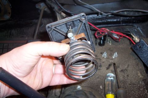 1973 Ford F-250 - A hand holds a black plastic housing with a large metal coil attached. Wires and screws are visible in the background, suggesting a vehicle…