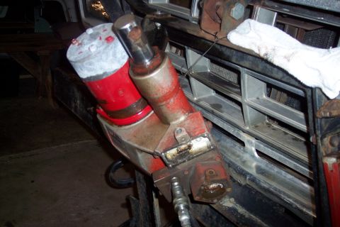 1973 Ford F-250 - A red and silver hydraulic jack is attached to the front grille of a vehicle, likely a truck, with a white cloth draped over the grille.