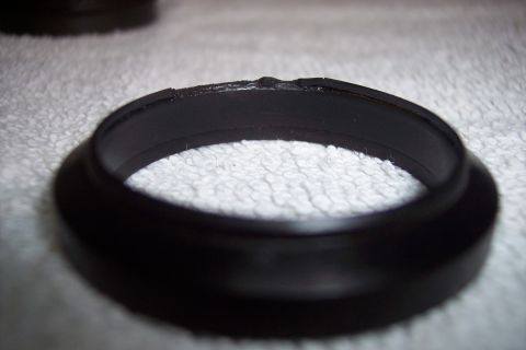 1973 Ford F-250 - A close-up, angled view of a damaged black rubber or plastic ring, possibly a seal or gasket, resting on a textured white surface. The top…