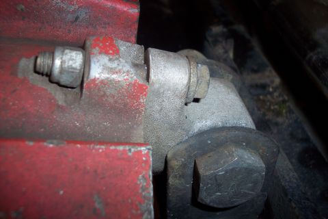 1973 Ford F-250 - A close-up view shows a heavy-duty metal bracket with a large bolt and nut assembly, painted red on one side and metallic gray on the other…