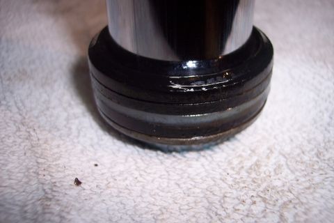 1973 Ford F-250 - A close-up view of the bottom of a chrome cylinder with black seals, resting on a white textured surface. There are some small dark debris…