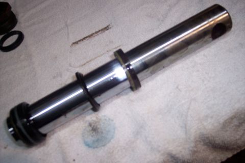 1973 Ford F-250 - A close-up view of a shiny metal piston or shaft with black rubber seals and a brass-colored ring. The part is resting on a white textured…