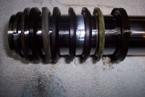 1973 Ford F-250 - A close-up view of a hydraulic cylinder rod with multiple worn seals and rings. The metal rod is shiny and appears to be part of a larger m…