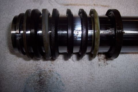 1973 Ford F-250 - A close-up, side view of a hydraulic cylinder rod with multiple worn seals and rings. The metal rod shows some scoring and wear marks.