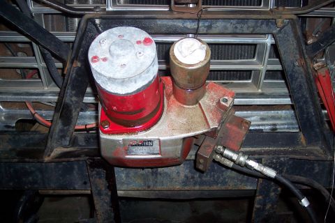 1973 Ford F-250 - A close-up view of a red and silver hydraulic pump mounted to the front of a vehicle, likely a truck, with a chrome grille visible in the b…