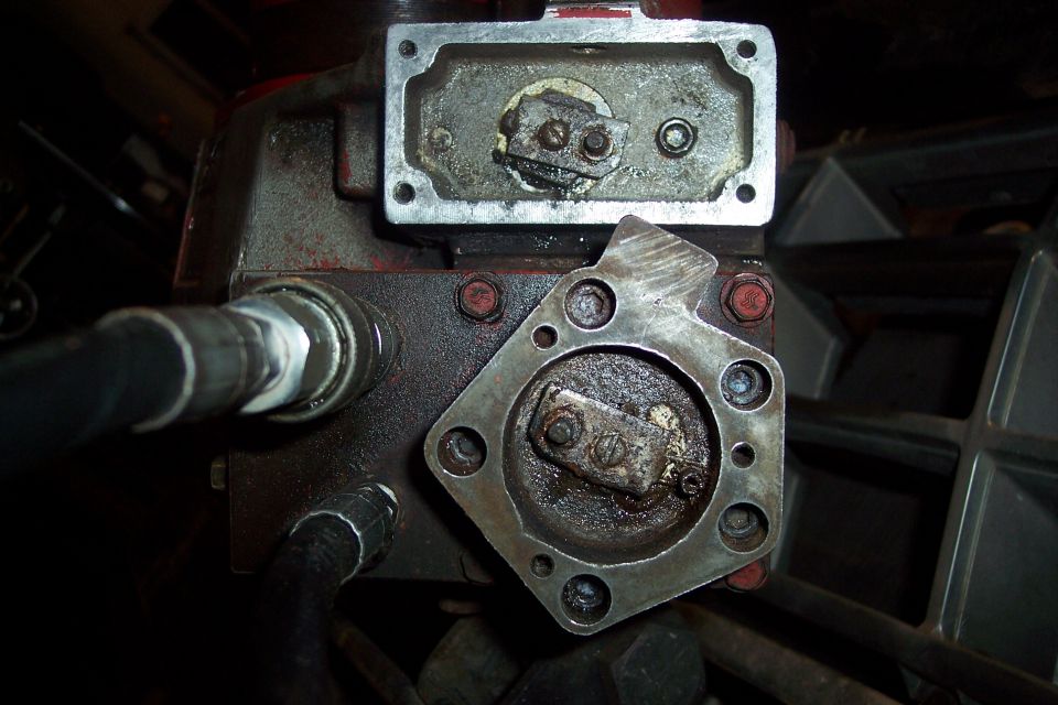Close-up of hydraulic pump components with hoses, showing oil and grime.