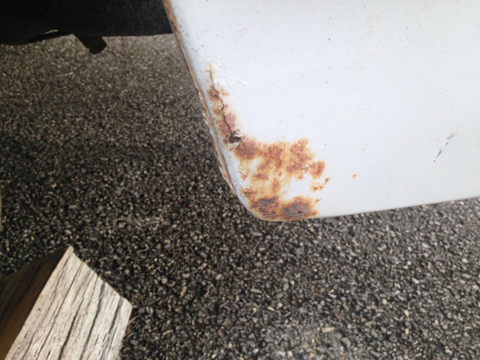 Rust forming on the white corner of a vehicle body panel over a gravel surface.