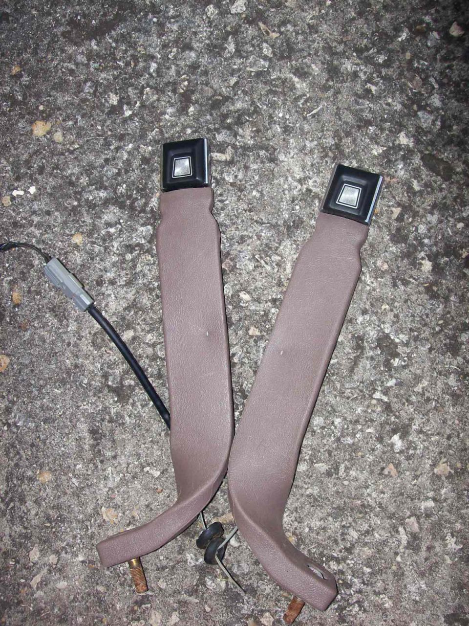 Two brown seat belt assemblies with black buckles on concrete.