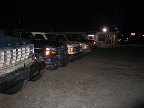 1995 Ford Bronco - Multiple trucks are parked in a line at a dimly lit location during the night.