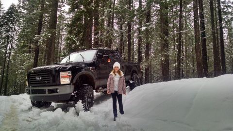 1985 Jeep CJ7 - A young girl stands in the snow next to a black Ford F-Series pickup truck in a snowy forest setting.