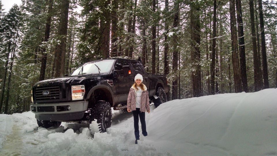 Girl standing next to a black Ford F-Series pickup truck in a snowy forest.