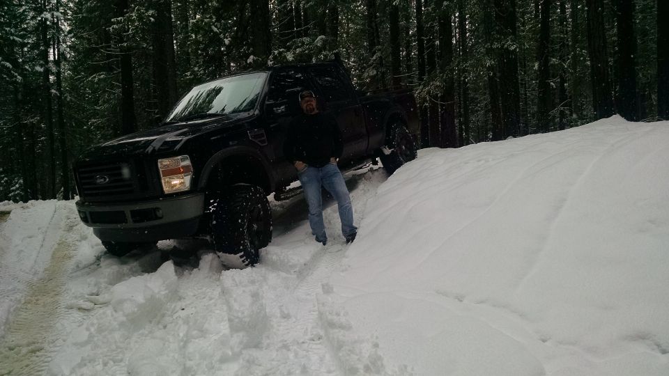 Man standing next to a black Ford F-Series pickup truck in a snowy forest.