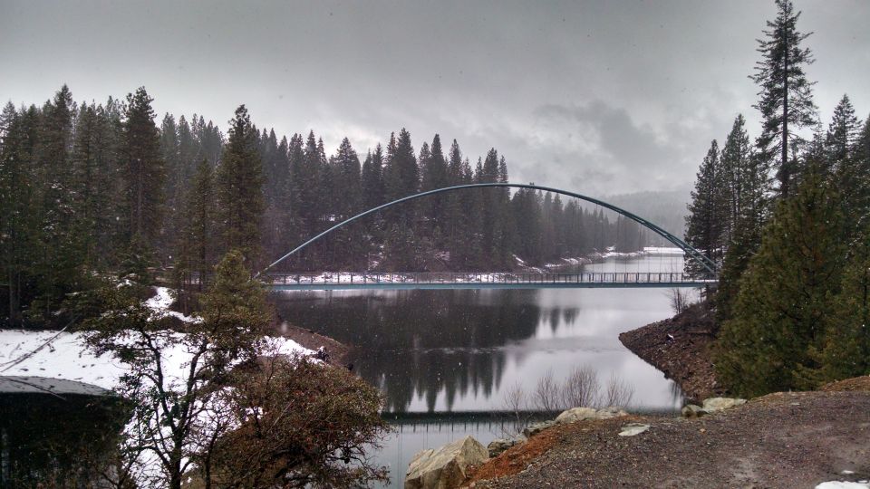 Arch bridge over water with pine trees and snow.