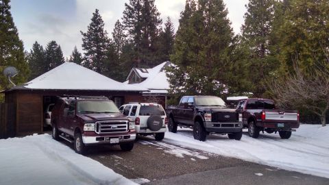 1985 Jeep CJ7 - A dark red Ford Excursion SUV is parked in front of a snow-covered garage, with a white Jeep Liberty and two Ford pickup trucks behind it.…