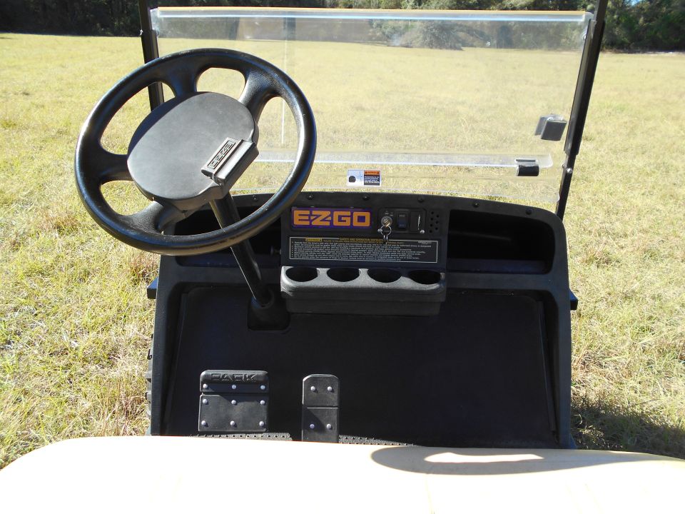 Golf cart interior with steering wheel, EZGO dashboard, and pedals.