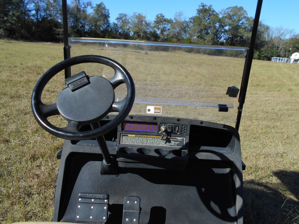 Golf cart interior with steering wheel, dashboard, and pedals.