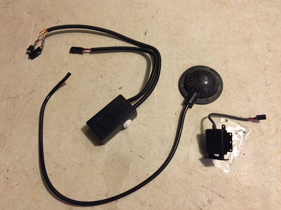 Electronic components including a control box, speaker/light, and a small box in a bag on a concrete surface.