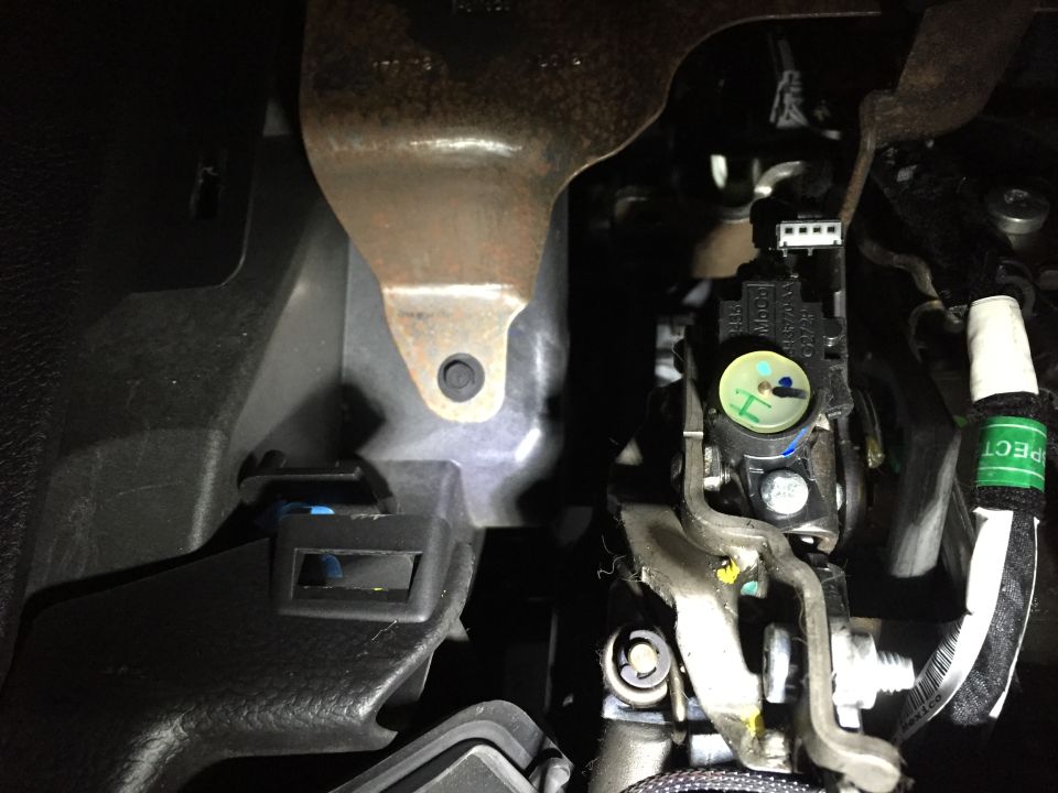 Close-up of vehicle brake pedal sensor with white connector and green label.