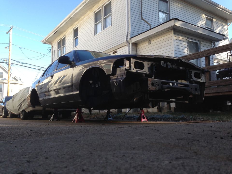 Dark sedan on jack stands with front end disassembled.