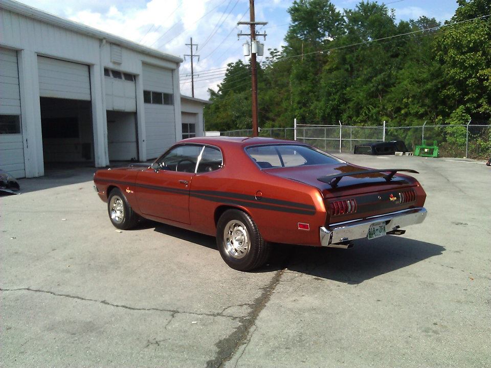 Copper 1971 Dodge Dart coupe with black stripes and spoiler parked in front of garage.