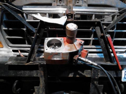 1973 Ford F-250 - A close-up, low-angle shot of the front of a truck grille with a hydraulic winch mechanism mounted in front of it. The mechanism is red and…