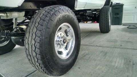 1979 Ford Bronco - A close-up, low-angle shot shows the massive off-road tire and polished chrome wheel of a lifted truck or SUV, with part of the vehicle's u…