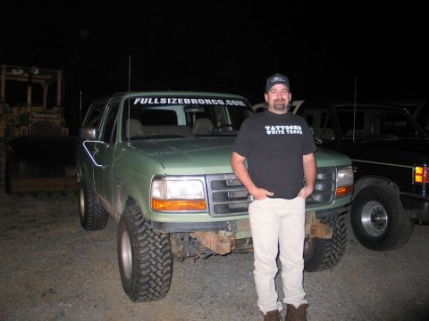 1995 Ford Bronco - A man stands in front of a green 1995 Ford Bronco, which has a website address displayed on its windshield.