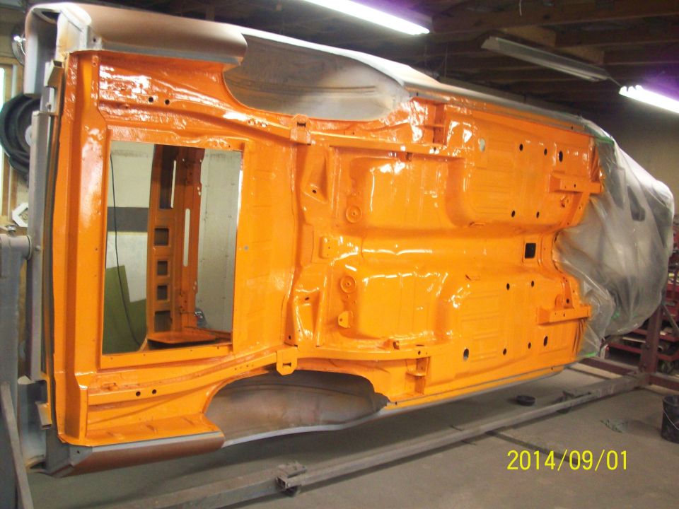 Upside down orange painted classic car body undergoing restoration