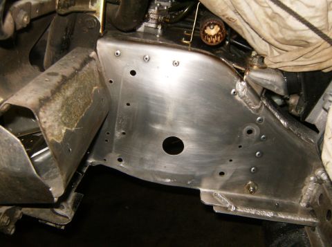 2000 Ford E350 - A close-up view of the underside of a vehicle's chassis, showing a custom-fabricated aluminum panel with numerous rivets and a central circ…