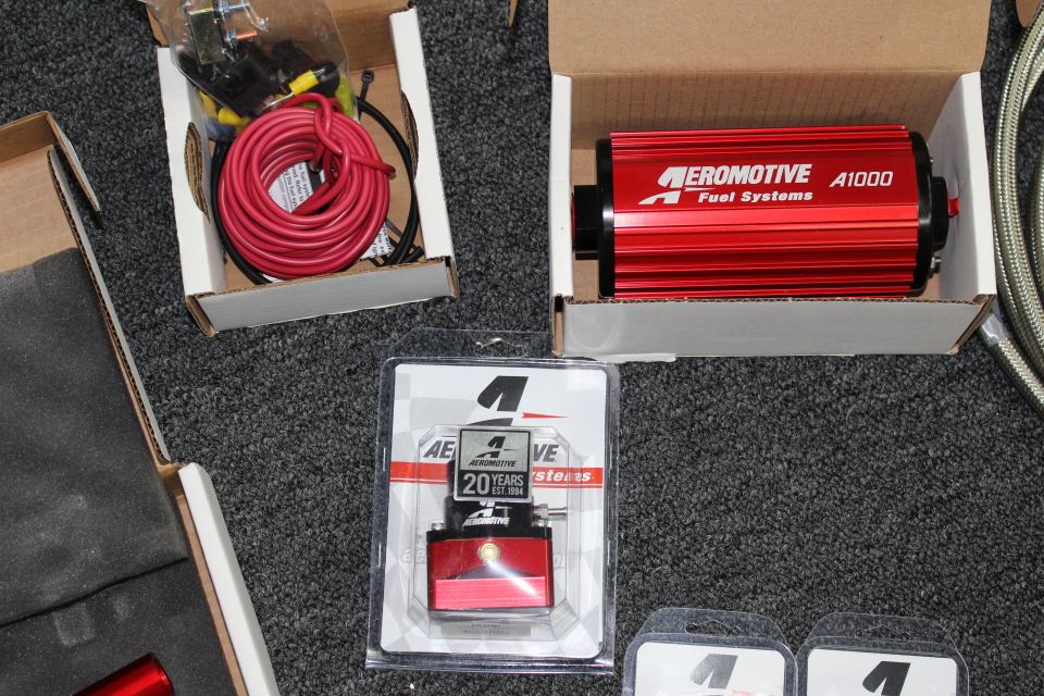 Red Aeromotive A1000 fuel pump in a box beside coiled red wire and a blister-packed red part