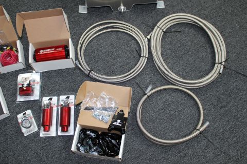 2003 Ford Crown Victoria - Three coils of braided stainless fuel line laid out next to boxed Aeromotive pump, regulator, gauge, and a box of black fittings.