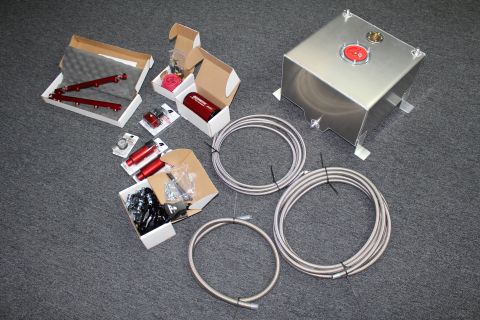 2003 Ford Crown Victoria - fuel system kit spread on gray carpet with an aluminum fuel cell, red rails and regulator, assorted fittings, and coils of braided line.