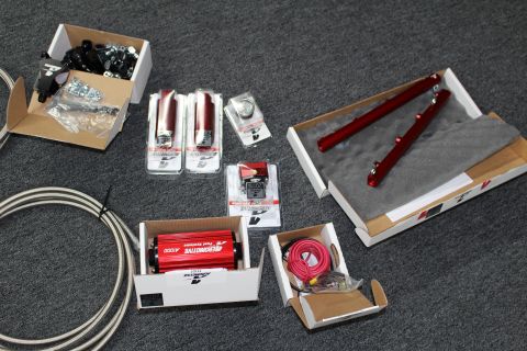 2003 Ford Crown Victoria - Boxed fuel system parts spread on carpet including black fittings, red gauges, a red Aeromotive A1000 pump, red rails or shocks, and coiled…