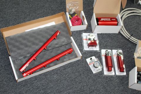 2003 Ford Crown Victoria - Fuel system parts arranged on carpet: red fuel rails in a foam box, a red A1000 pump, regulator, pressure gauge, and blister-packed red fit…