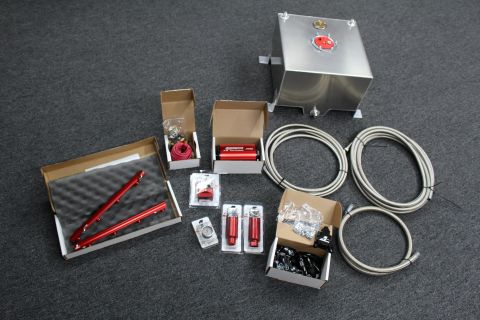 2003 Ford Crown Victoria - fuel system kit laid out on carpet with an aluminum fuel cell, red rails, regulator, a box of fittings, and coils of braided line.