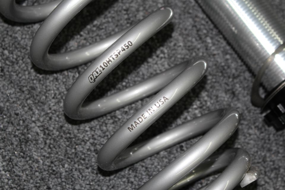 Close-up of gray coil spring stamped QA110HTSF450 and MADE IN USA beside shock body