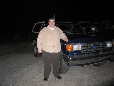 1995 Ford Bronco - A man poses with a dark blue SUV, which appears to be from the 1980s, in a gravel lot at night.