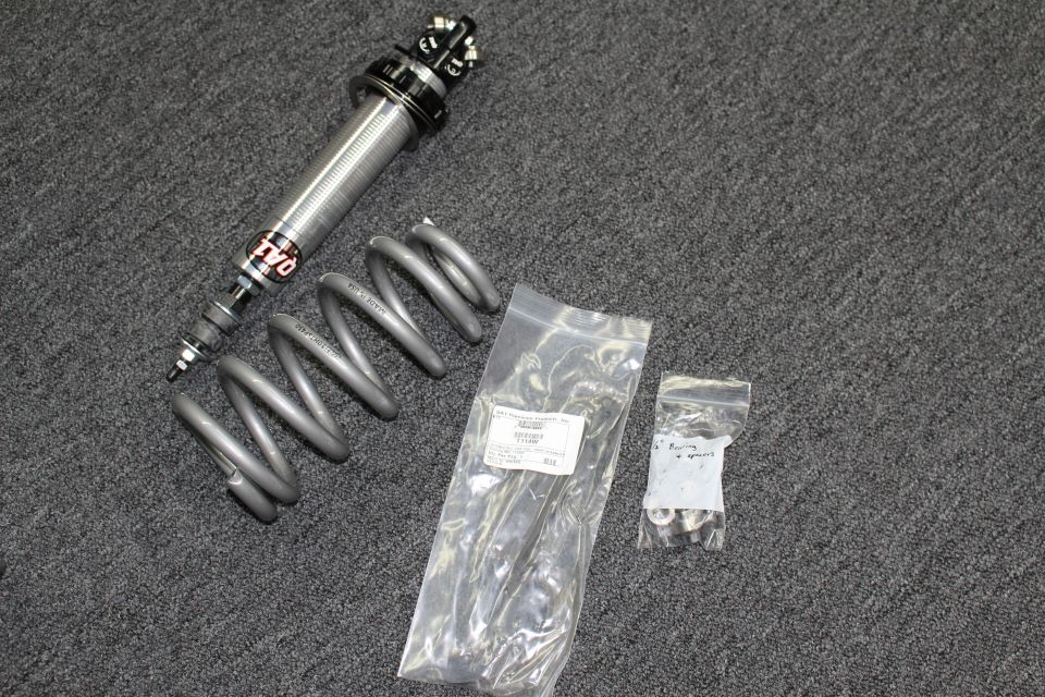 QA1 coilover shock with gray coil spring and two bags of hardware on carpet