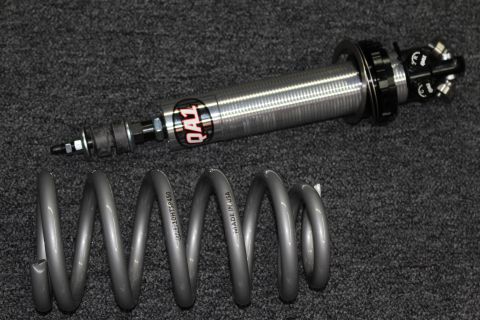 2003 Ford Crown Victoria - QA1-branded coilover shock absorber positioned above its gray coil spring on dark gray carpet.