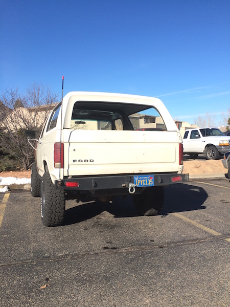 1981 Ford Bronco - Rear view of a white Ford Bronco with a custom bumper and aftermarket wheels.