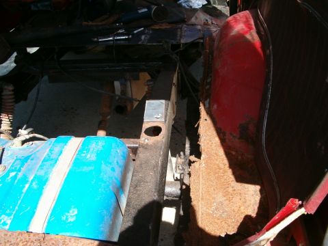 1979 Ford Bronco - Close-up view of a blue fuel tank with white stripes, situated near a rusty vehicle frame.