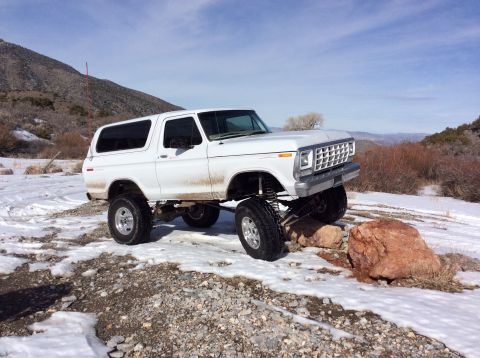 1979 Ford Bronco - White lifted Ford Bronco navigating rocky terrain with snow on the ground.