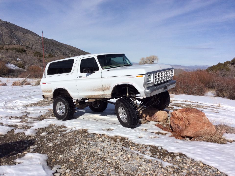 White lifted Ford Bronco driving over rocks in a snowy, mountainous area