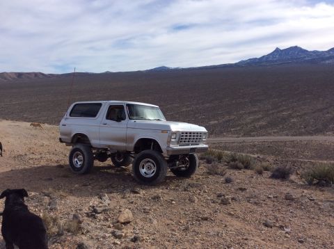 1979 Ford Bronco - A lifted 1979 Ford Bronco sits on a dusty trail with mountains in the background.