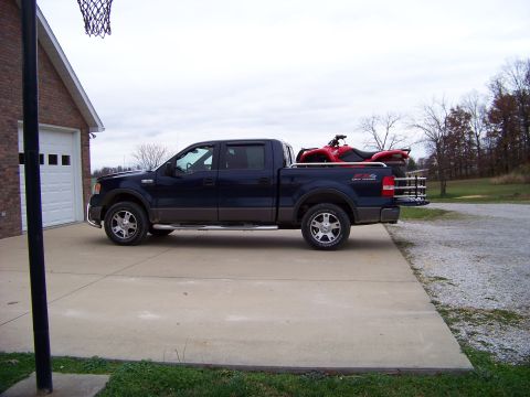 1984 Honda ATC 250 R - A dark blue pickup truck is parked in a driveway next to a brick garage, with a red ATV loaded in its bed.