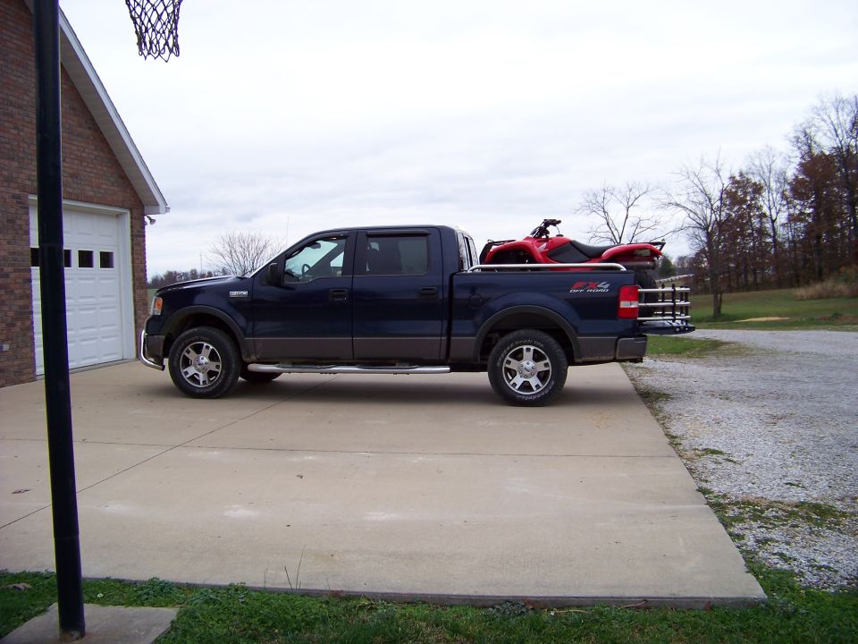 Dark blue pickup truck parked in driveway with a red ATV in the bed