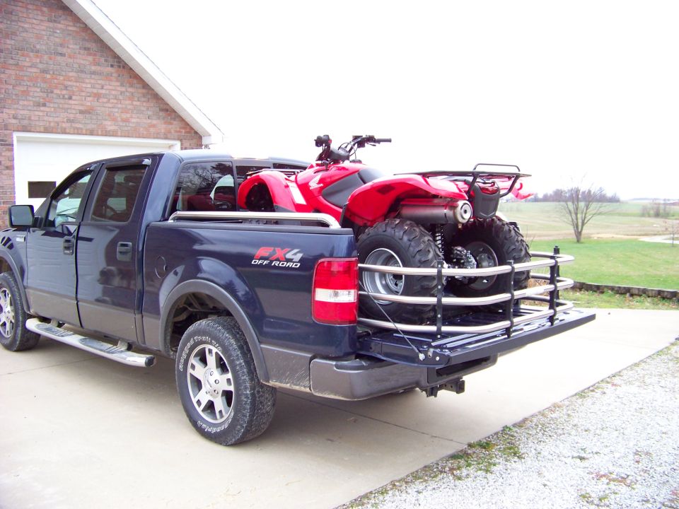 Red ATV loaded in the bed of a dark blue pickup truck with a metal rack